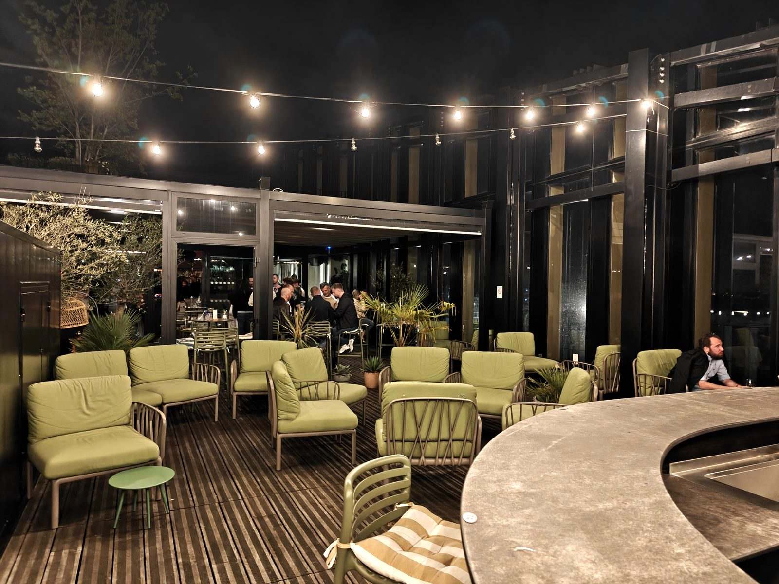 Terrasse du rooftop du Mesa de nuit, fauteuils verts et guirlandes lumineuses